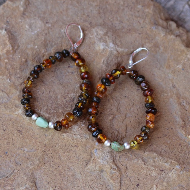 Flexible hoop earrings with amber beads and a single turquoise bead framed with sterling silver beads. Sterling silver lever back ear wires.