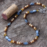 Blue kyanite ovals necklace with golden freshwater pearls, mocha Swarovski crystals, and amber.  Cork shows size reference.