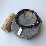 Stretch necklace or triple wrap bracelet with navy blue seed beads, garnet Swarovski crystals, and a sterling silver I heart you charm. Cork for size reference