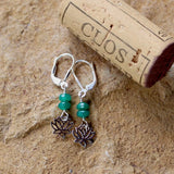 Earrings with little sterling lotus charms and emerald beads on sterling silver lever back ear wires. Cork for size reference.