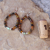 Amber beaded flexible hoop earrings with a turquoise bead framed with satin-finish sterling beads. Sterling lever back ear wires keep the earrings secure. Cork shown for size reference.
