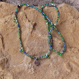 Stretch necklace or triple wrap bracelet with sterling tiny heart charm and a mix of blue and green seed beads. Green glass drop beads are interspersed along the strand.